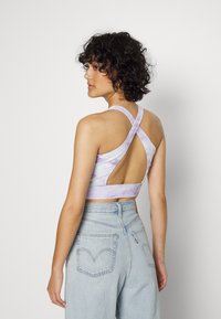 Top crop tie-dye roxo com alças cruzadas e costas abertas. Combinado com jeans de cintura alta em lavagem clara com bolsos traseiros.