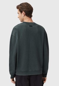 Felpa verde scuro con vestibilità rilassata, polsini e orlo a costine, con un discreto dettaglio dell'etichetta sul collo posteriore. Tessuto dalla texture morbida.