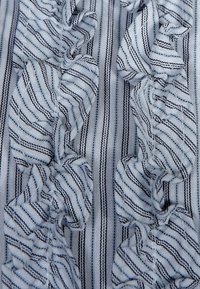 Tissu à rayures bleues et blanches avec des détails en volants. Les rayures sont fines et espacées de manière régulière, créant un effet visuel texturé.