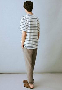 Camiseta de rayas blancas y marinas, de corte relajado, combinada con joggers gris claro. Zapatos marrones de tipo slip-on, mostrados desde la parte trasera contra un fondo liso.