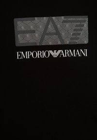 Camiseta de algodón negra con un estampado gráfico texturizado en blanco con patrones hexagonales y el logo de "Emporio Armani" en la parte inferior.