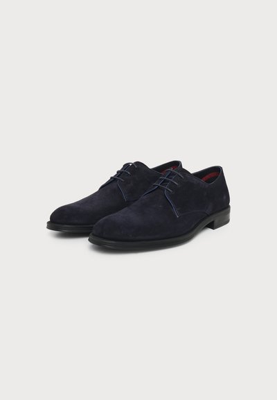 Paire de chaussures habillées pour homme en daim bleu foncé avec semelles et lacets noirs, présentée côte à côte sur un fond clair uni.