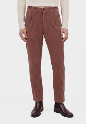 Pantaloni di velluto a coste marroni indossati con stivaletti in pelle marrone scuro e una maglia beige a maniche lunghe, mostrati dalla vita ai piedi.