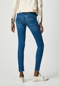 Skinny blue denim jeans with a high waist, two back pockets, and a slightly faded finish, paired with white sneakers.