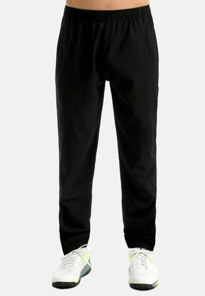 Pantalones jogger con cintura elástica negra, usados con zapatillas blancas y verde neón, mostrados desde la cintura hasta los pies sobre un fondo liso.