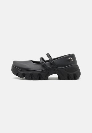 Zwarte klompen met een glad upper van synthetisch materiaal, twee verstelbare banden en een dikke, gestructureerde zool met een golfpatroon.