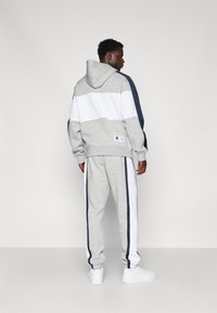 Sudadera con capucha en bloques de color gris y blanco, con acentos en azul marino, combinada con pantalones grises con rayas laterales, luciendo zapatillas blancas.