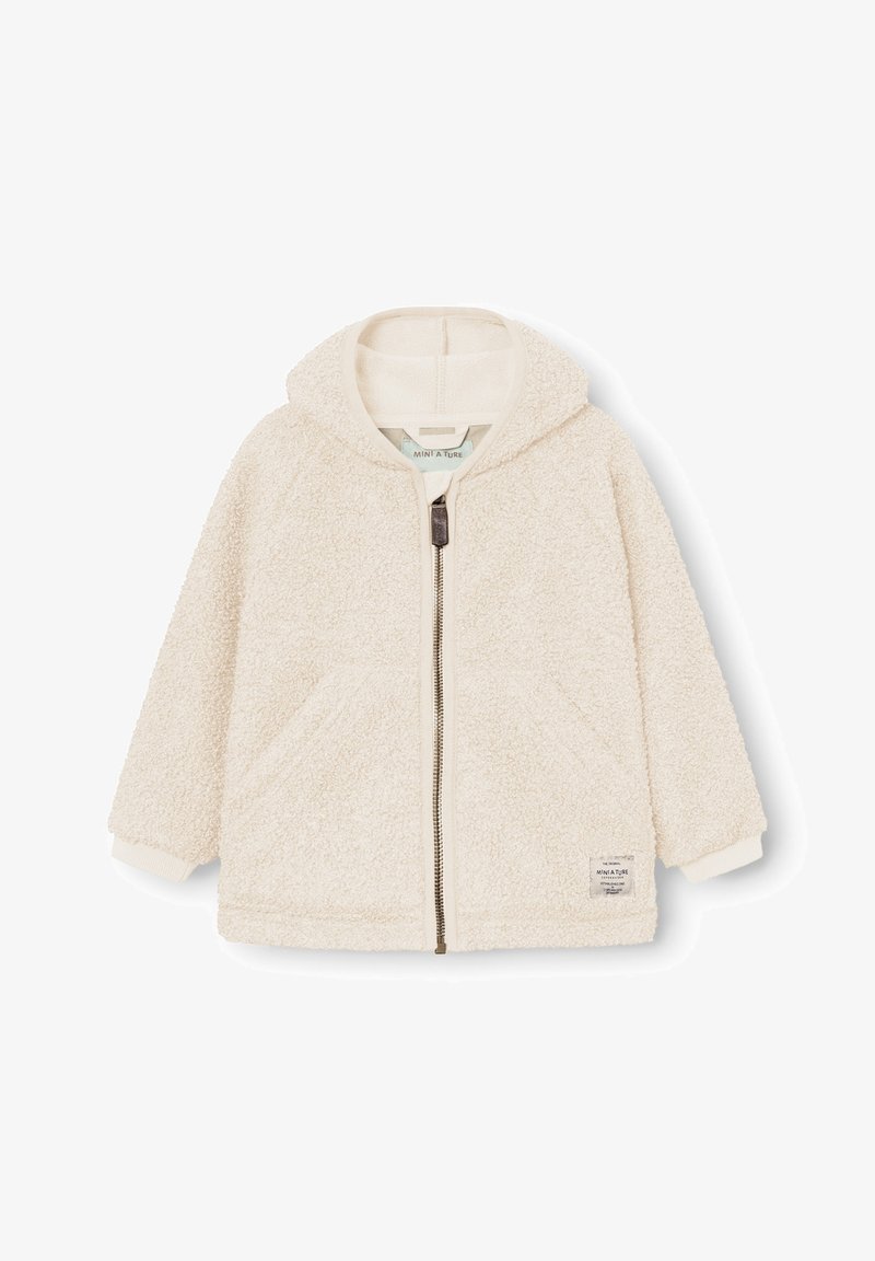 Veste à capuche en polaire couleur crème avec fermeture éclair devant, deux poches, poignets côtelés et une petite étiquette près de l'ourlet du côté gauche.
