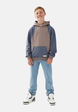 Hættetrøje med et beige og blåt farveblokdesign. Af bomuldsmateriale, med en frontlomme, ribstrikkede manchetter og kant. Båret med lyse jeans og sneakers.