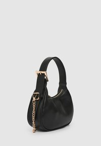 Schwarze Lederhandtasche mit geschwungener Silhouette, ausgestattet mit einer goldfarbenen Kettenverzierung und einem Reißverschluss. Der Griff ist verstellbar.