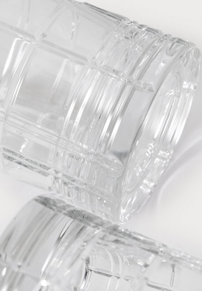 Caurspīdīgi plastmasas dzeramie glāzes ar režģa rakstu, cilindriskas formas, gluda tekstūra un noapaļotas malas, sakārtotas daļēji pārklājoties.