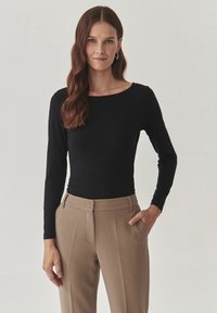 Zwarte longsleeve top met een bootnek, gecombineerd met beige op maat gemaakte broeken. Gladde stof, figuurvolgend ontwerp en minimale hardwaredetails.