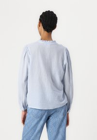 Blusa a righe blu chiaro con colletto arricciato, maniche lunghe a palloncino e vestibilità morbida, abbinata a jeans blu testurizzati con motivo a serpente.