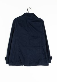 Námornícky modrá bavlněná bunda s límcem, zapínacími manžetami a dvěma předními kapsami, zavěšená na černém háčku na bílém pozadí.