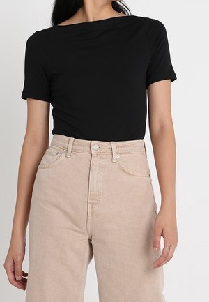 Top nero a maniche corte con scollatura ampia, abbinato a jeans chiari beige a vita alta, con chiusura a zip e bottone.