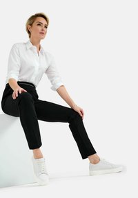 Witte blouse, zwarte slim-fit broek en witte sneakers. Onderwerp zit ontspannen met een relaxte houding en toont een minimalistische stijl.