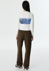 Witte lange mouw top met een blauwe denimprint op de achterkant, gecombineerd met een paarse bruine wijde broek. Glad textuur en relaxte pasvorm.