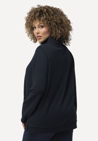 Tmavě modrý svetr s vysokým límcem, dlouhými rukávy a bočními rozparky na spodním okraji. Měkká tkanina s hladkým povrchem.