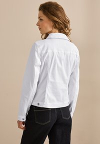 Vit denimjacka med en figursydd design, långa ärmar, knappryck och detaljer på ryggen. Matchad med mörka denimbyxor.