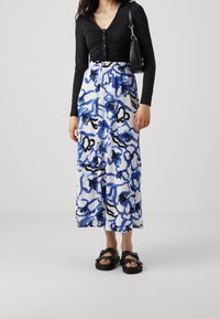 Černý dlouhý rukáv s knoflíky vpředu, kombinovaný s bílou midi sukní s modrými a černými abstraktními vzory. Černé sandály s přezkami.