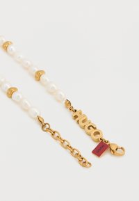 Κολιέ από μαργαριτάρια με χρυσές λεπτομέρειες, που διαθέτει μαργαριτάρια ακανόνιστου σχήματος, χρυσές χάντρες και χρυσό κούμπωμα με ετικέτα λογότυπο. Απλός σχεδιασμός.