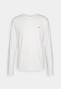 T-shirt blanc à manches longues avec col rond et petit logo brodé sur la poitrine gauche, présenté sur un fond uni gris clair.