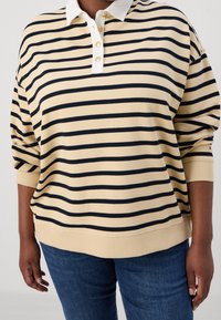 Sudadera tipo polo de rayas beige con líneas horizontales en azul marino, cuello blanco y botones dorados. Presenta puños y dobladillo acanalados. Ajuste casual.