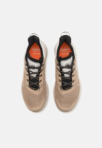Baskets de sport beiges avec accents noirs, surface texturée, design perforé et semelles intérieures orange contrastantes. Dotées de lacets noirs et d'un logo.