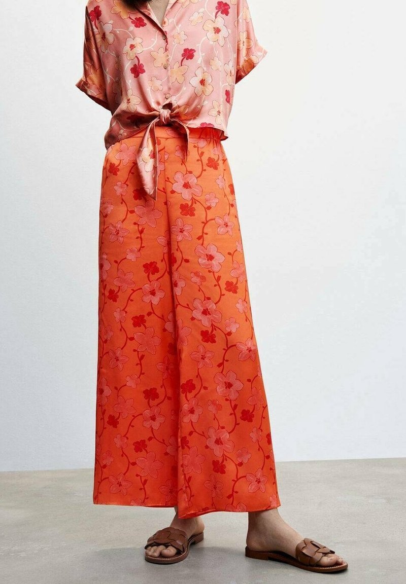 Bloem blouse in roze en oranje met korte mouwen, gecombineerd met oranje, met bloemenpatroon wijde broek met rode en roze bloemen. Bruine sandalen.