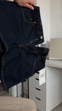 Dunkelblaue Denim-Shorts mit einem Reißverschlussfach, fünf Taschen, kontrastierenden Nähten und einem Metallknopfverschluss. Anhänger mit dem Code D62 befestigt.