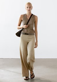 Bruine mouwloze top, beige gestreepte wijde broek, zwarte sandalen en een donkere schoudertas. Eenvoudig ontwerp met subtiele texturen.