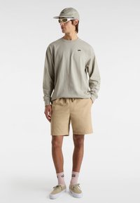 Lysegrå skjorte med lange ærmer og lille logo, beige shorts med snøre, khaki cap, grøntönede solbriller og lyserøde sokker med logo.