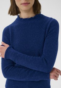 Modrý pletený sveter vyrobený z mäkkej, textúrovanej tkaniny, s okrúhlym výstrihom so zvlneným lemom a dlhými rukávmi.