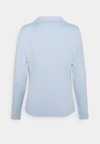 Blazer de manga larga azul claro con cuello con muesca, costuras visibles en la parte trasera y silueta entallada, mostrado desde atrás sobre un fondo blanco.