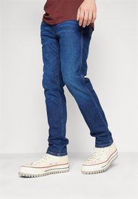 Modre jeans hlače s ožjim krojem, nosene z off-white visokimi supergami z teksturirano podplatom in rdečim trakcem.