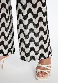 Hoge taillebroek met een golvend zwart-wit patroon, gemaakt van textuurstof. Gecombineerd met strappy witte hoge hakken.