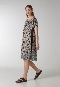 Lyhythihainen mekko, jossa on geometrinen vaaleanbeige ja musta kuvio, jossa on seeprahäntä. Valmistettu kevyestä kankaasta, jossa on rento istuvuus.