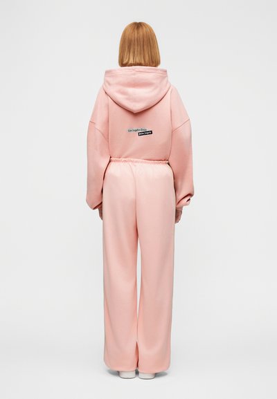 Σετ με ροζ φούτερ με κουκούλα και παντελόνια φαρδιάς γραμμής, κατασκευασμένο από απαλό ύφασμα. Το φούτερ διαθέτει ετικέτα με λογότυπο στην πλάτη. Άνετη γραμμή, casual σχεδιασμός, μαλακή υφή.