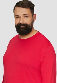 Rotes Langarmshirt aus weichem Stoff, mit Rundhals und lockerer Passform, vor einem einfarbigen grauen Hintergrund.