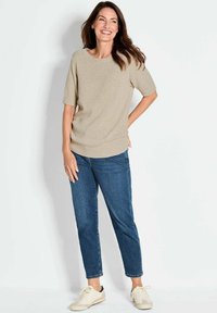 Maglione beige a maglia con scollatura rotonda e maniche corte, abbinato a jeans in denim blu e sneakers color crema. Texture liscia, vestibilità comoda.