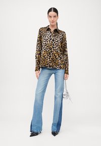 Košeľa s leopardím vzorom v hnedých a čiernych tónoch, plochý golier, predné gombíky. Svetlo modré rozšírené džínsy s kombinovanými odtieňmi denimu. Čierne špicaté topánky, strieborná kabelka.