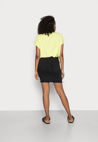 Zwarte denim mini-rok met een rafelige zoom, gecombineerd met een losvallende felgroene shirt. De schoenen zijn zwarte sandalen met een kurken zool.