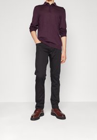 Dunkellila Langarm-Poloshirt mit Kragen, kombiniert mit schwarzen Slim-Fit-Hosen und braunen Schnürschuhen, von der Taille abwärts gezeigt.