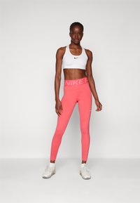 Reggiseno sportivo bianco e leggings rosa brillante con ampia cintura e logo "NIKE". L'outfit è realizzato in materiale elastico, ideale per l'abbigliamento sportivo.