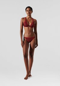Bikini komplektas gilia raudona spalva. Triangulinis bikini viršus su plonomis petnešomis ir subtiliu raštu. Žemas bikini apatinis trikotažas su atitinkama juosta. Lygus paviršius.