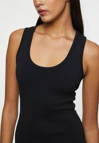 Sort ærmeløs tanktop med en rund halsudskæring. Lavet af glat, strækbart stof, som har et tætsiddende design, der følger kroppens konturer.