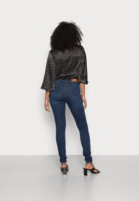 Svart satin topp med vita prickar, utsvängda ärmar, matchad med mörkblå slim-fit jeans. Modell som bär svarta klacksandaler.