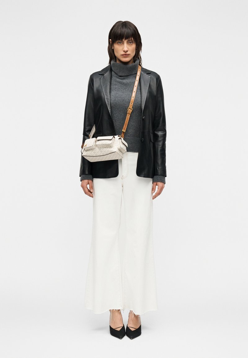 Μαύρο δερμάτινο σακάκι, γκρι ζιβάγκο, λευκό παντελόνι με φαρδύ πόδι και άγρια τελειώματα, μαύρες μυτερές γόβες και μια κρεμ τσάντα χιαστί με υφή και καφέ λουρί.