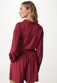 Bordeaux, leichtes Stoffhemd und Shorts-Outfit. Das Hemd hat einen Kragen, lange Ärmel mit Knopfmanschetten, elastischer Bund an den Shorts.