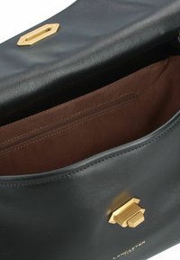 Zwarte leren tas met een gouden hexagonale sluiting, met een bruine binnenkant en een ritsvak aan de zijkant. Glad textuur, gestructureerde vorm.